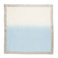 The Kim Seybert Dip Dye Napkin Set by Kim Seybert features a square cloth with a beige border and a dip-dye effect, transitioning from cream to light blue, evoking subtle autumn colors.
