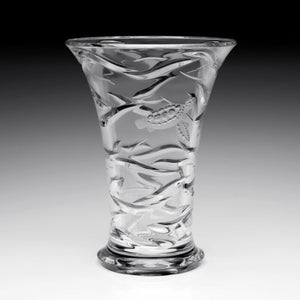 The Persephone Vase by William Yeoward Crystal is a clear glass piece with a flared rim, featuring engraved raised fish and wavy patterns that evoke the graceful movement of sea creatures.