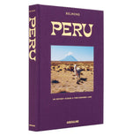 Peru, An Odyssey Across a Time Honored Land" by Assouline is a hardcover book with a purple cover featuring a llama in front of mountains and a volcano—ideal inspiration for Peru travel or dreaming of Machu Picchu.