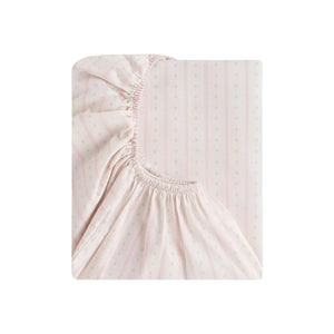 The Gooselings Petal Scallop Bedding is a folded pale pink crib sheet with a subtle dotted and striped pattern, partly revealing its elasticized edge. Made from OEKO-TEX certified cotton sateen for gentle comfort.