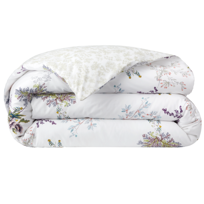The Naiades Bedding Collection by Yves Delorme features a folded white comforter with a vibrant floral print and a lighter, subtly patterned underside—crafted from organic cotton for added softness and comfort.