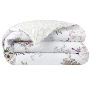 The Naiades Bedding Collection by Yves Delorme features a folded white comforter with a vibrant floral print and a lighter, subtly patterned underside—crafted from organic cotton for added softness and comfort.