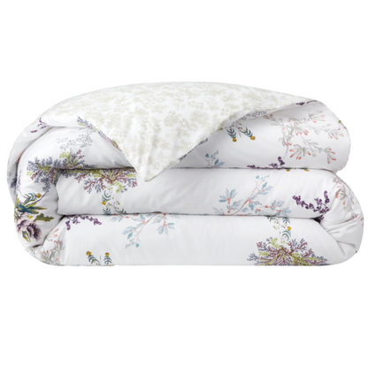 The Naiades Bedding Collection by Yves Delorme features a folded white comforter with a vibrant floral print and a lighter, subtly patterned underside—crafted from organic cotton for added softness and comfort.