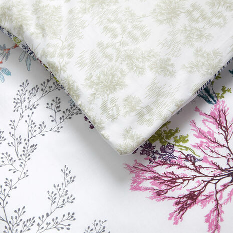 Close-up of the Naiades Bedding Collection reversible duvet cover by Yves Delorme, made in France, featuring a botanical print with light green, gray, and pink leafy branches on a white background.