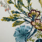 The Naiades Bedding Collection by Yves Delorme features botanical green and yellow foliage, blue and maroon flowers, and a light insect with red-tipped wings—perfect for a reversible organic cotton duvet cover.
