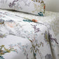 A neatly made bed features Yves Delorme's Naiades Bedding Collection—white sheets and pillowcases with colorful botanical prints, plus an organic cotton reversible duvet cover made in France.