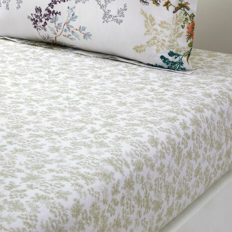 A close-up of the Naiades Bedding Collection by Yves Delorme: a neatly made bed featuring a white fitted sheet with green leaf patterns, a floral pillowcase, and an organic cotton reversible duvet cover—crafted for comfort.