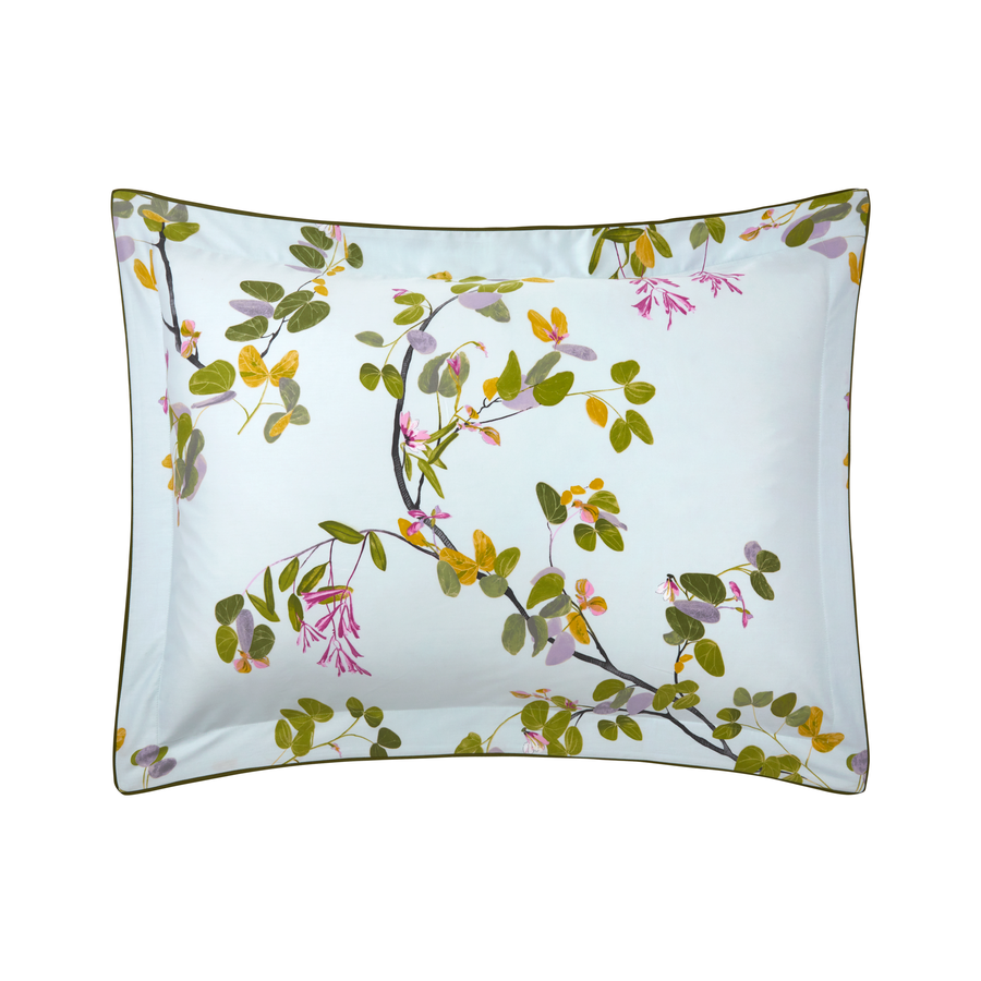 A rectangular pillowcase from Yves Delorme’s Luciole Bedding Collection, made of organic cotton sateen, features green leaves and pink flowers on a light blue background.