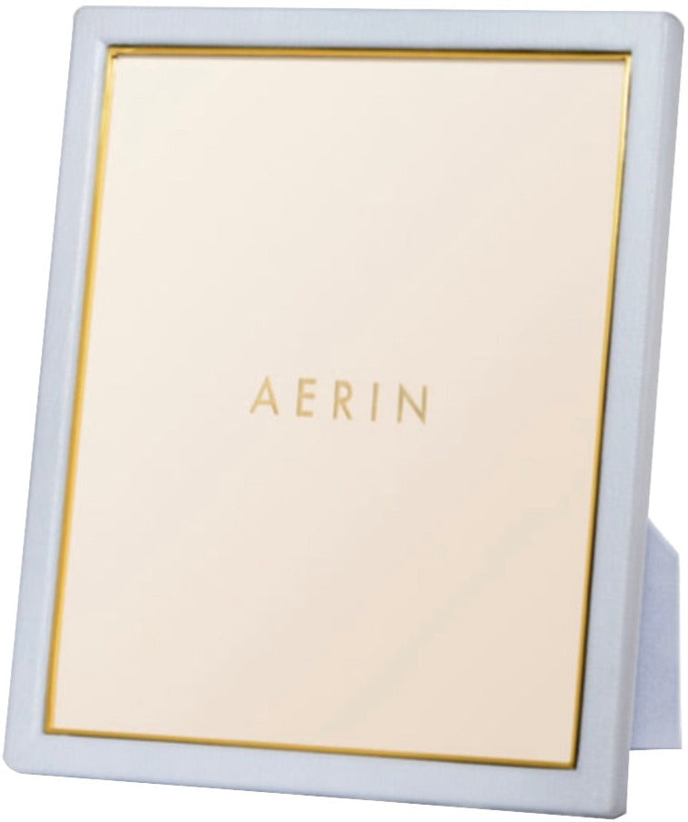 The Aerin Piero Leather Frame Collection features a rectangular frame with a white leather border and gold detailing, standing upright for an elegant display on any flat surface. The brand name "AERIN" is displayed in the center.