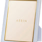 The Piero Leather Frame Collection by Aerin features a white frame with gold detailing, a gold inner border, and a stand for elegant display. The included placeholder card is labeled "AERIN.
