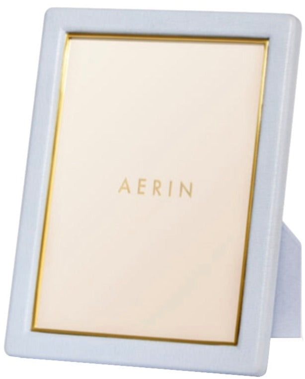 The Piero Leather Frame Collection by Aerin features a white frame with gold detailing, a gold inner border, and a stand for elegant display. The included placeholder card is labeled "AERIN.