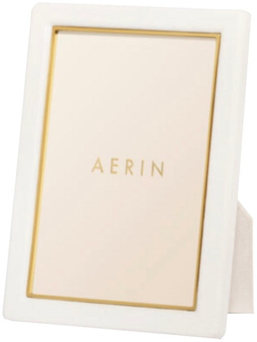 Aerin's Piero Leather Frame Collection features a white rectangular photo frame with gold detailing and a gold inner border, showcasing “AERIN” in gold at the center for an elegant display.