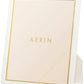 A white Piero Leather Frame from Aerin with gold detailing, featuring the brand’s name in the center, displayed upright for an elegant look.