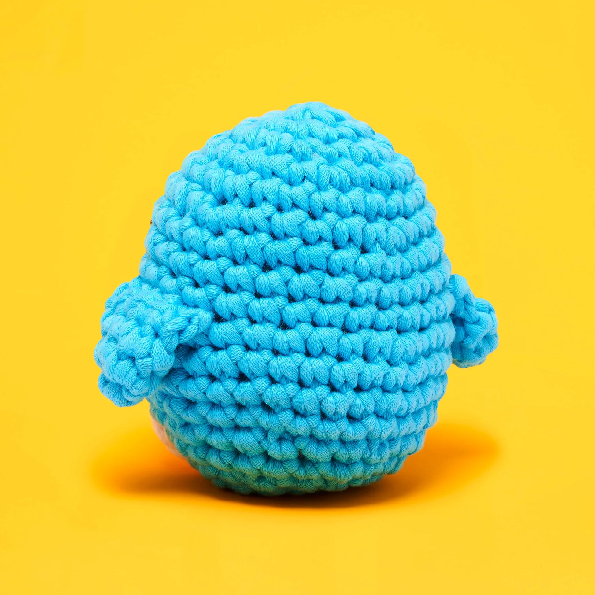 A blue, round figure with two small side flippers—Pierre the Penguin from The Woobles—rests on a solid yellow background, making this Beginner Crochet Kit perfect for anyone new to crochet or curious about the woobles style.