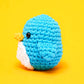 Pierre the Penguin Beginner Crochet Kit by The Woobles features a crocheted blue penguin with a white belly and yellow beak, set against a bright yellow background—perfect for beginner crochet enthusiasts or fans of The Woobles’ charming style.