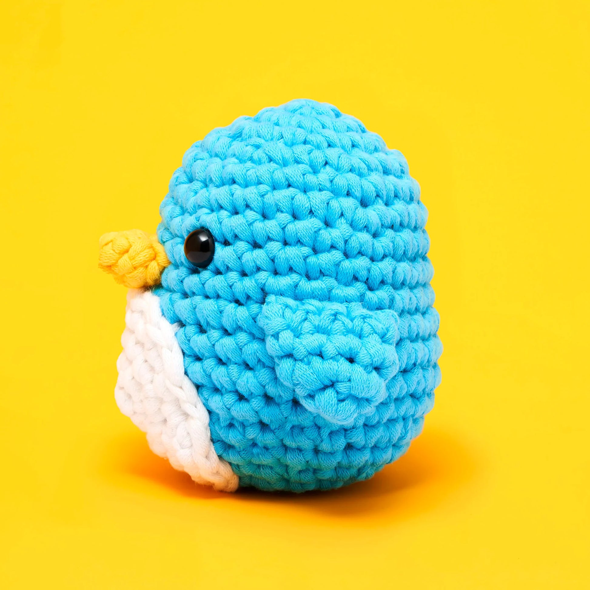 Pierre the Penguin Beginner Crochet Kit by The Woobles features a crocheted blue penguin with a white belly and yellow beak, set against a bright yellow background—perfect for beginner crochet enthusiasts or fans of The Woobles’ charming style.