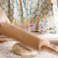 Person rolling out dough with a wooden rolling pin on a floured surface, dressed in a patterned apron and peach-colored sweater—just as taught by Kate Lebo in Pie School from Penguin Random House, mastering techniques for irresistibly delicious pies.