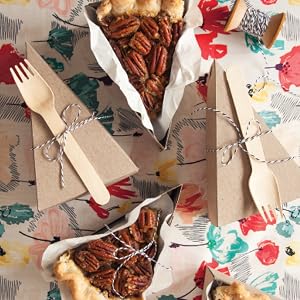 Three slices of pecan pie, each wrapped in parchment paper and tied with string, are arranged alongside compostable cutlery on a vibrant floral-patterned surface—a setting evocative of the delicious recipes featured in Pie School by Penguin Random House.