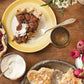 A wooden table adorned with an array of pies, plates holding pie slices, bowls of whipped cream, blueberries, flowers, and gold utensils arranged for serving—an inviting scene reminiscent of the mouthwatering creations featured in Pie School by Penguin Random House, perfect for anyone looking to discover inspiring pie recipes.