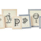 The Pigeon & Poodle Aberdeen Frame Collection by Pigeon & Poodle is a set of six framed prints of vintage illustrations, featuring designs such as a hot air balloon, a diver, a palm tree, and ornate letter motifs. The frames are crafted from Narra veneer wood in neutral-colored hues.