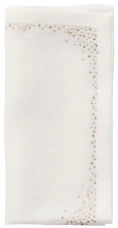 The Kim Seybert Pin Dot Napkin Set features a folded white napkin with a decorative border of small gold and silver dots along two adjacent edges, offering an elegant design.