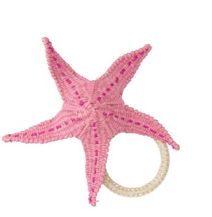 The Mercedes Salazar Starfish Napkin Ring Collection features a pink starfish-shaped woven ornament with a circular handle, crafted from natural rattan, perfect for unique table settings.