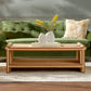 The Matthew Coffee Table by Made Goods, featuring a unique light wood design and a decorative vase, is placed on a cream rug in front of a green sofa with a beige fur pillow.