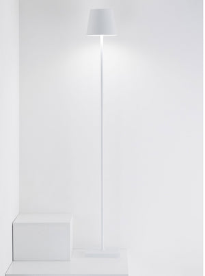 The Zafferano America Poldina Pro L Floor Lamp stands on a white floor by two white cubes against a plain wall, offering cordless convenience and touch dimming.