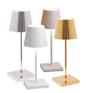 The Zafferano Poldina Pro Mini Table Lamp Collection by Zafferano America features four touch dimmable LED lamps with cone-shaped shades and square bases in white, silver, beige, and gold. Ideal for indoor or outdoor use, these portable rechargeable lamps blend style with functionality.