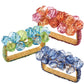 Three rectangular Kim Seybert Pop Rocks Napkin Rings feature gold bands with clusters of large faceted beads in pink-orange, blue-green, and light blue-purple, creating a sparkling, bejeweled design.