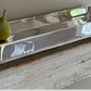 Two green pears sit on the Hôtel Silver Gallery Tray with Bun Feet & Cut-Out Handles, displayed on a rustic wooden shelf against a neutral wall.
