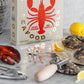 The PrintWorks Seafood Tool Set includes oysters, an oyster knife, shell cracker, lobster claw tool, lemon wedges, and comes in a box labeled "Seafood Tools," all arranged elegantly on a marble surface.