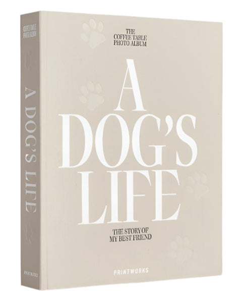 The image shows a beige dog photo album titled "A Dog's Life: The Story of My Best Friend" on the cover. This PrintWorks A Dog's Life Photo Album by PrintWorks features a cotton fabric cover and is crafted with high-quality photo paper.