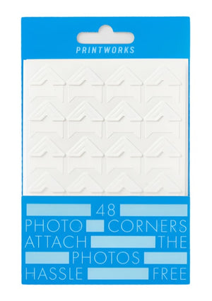 PrintWorks Photo Stickers: Pack of 48 acid-free, matte white, stick-on photo corners with eco-friendly adhesive, neatly arranged in rows and packaged in a blue and white cardboard box.