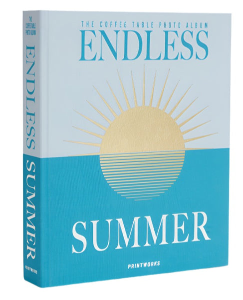 The "PrintWorks Endless Summer Photo Album" by PrintWorks features a turquoise cloth cover with a gold sun illustration and the words "The Coffee Table Photo Album" at the top, crafted with high-quality photo paper to preserve your cherished memories.