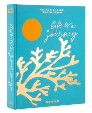 A turquoise cloth photo album titled "Life Is A Journey" by PrintWorks, with gold coral design and orange circle, features high-quality black photo paper. Known as the Coffee Table Photo Album.