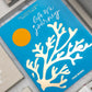 The PrintWorks Life Is A Journey Photo Album features a turquoise cloth cover with a gold coral design and yellow circle, shown among other books on a white surface.