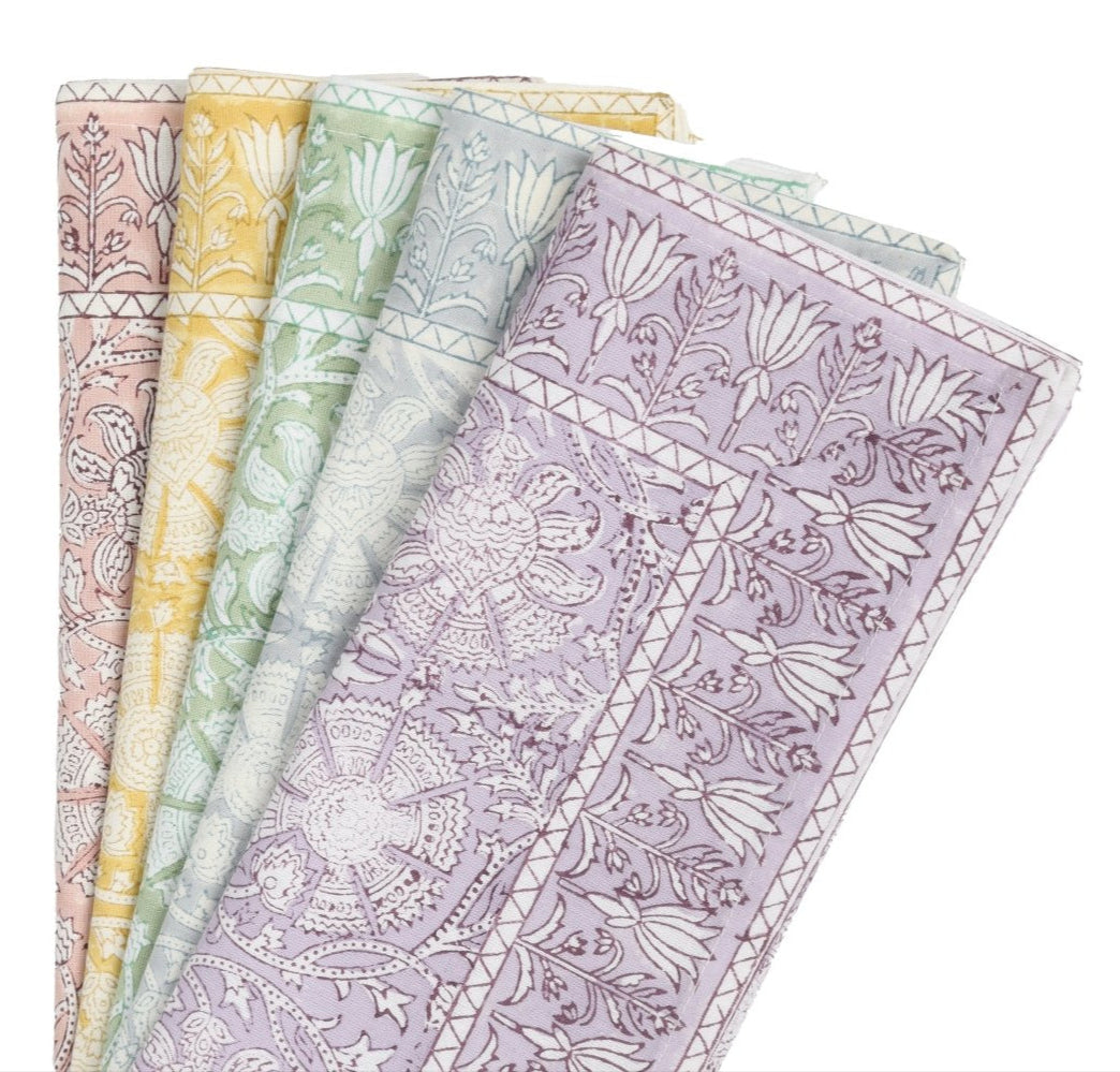 Five folded pieces of fabric with playful floral and geometric patterns in pastel pink, yellow, green, blue, and purple are arranged in a fan shape—perfect for pairing with the Kim Seybert Provence Napkin Set.