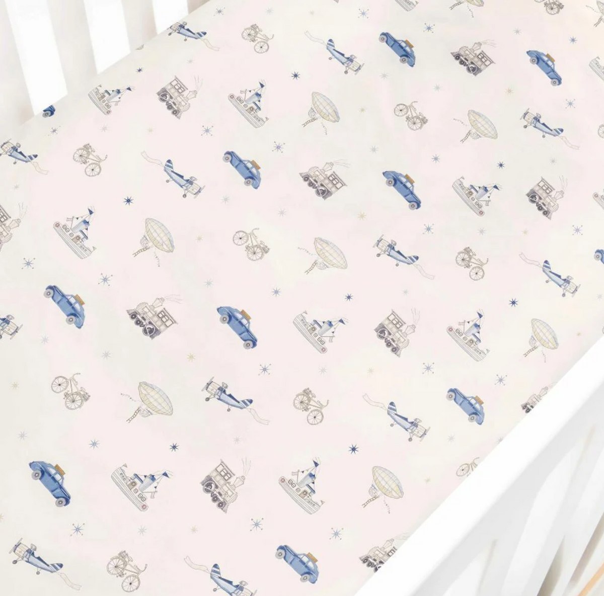 The Transit Treasures Bedding Collection by Gooselings features a breathable white crib sheet, crafted from pure materials and adorned with a repeating pattern of blue cars, bicycles, circus tents, animals, and hot air balloons in muted tones. For your peace of mind, this crib sheet is OEKO-TEX certified.