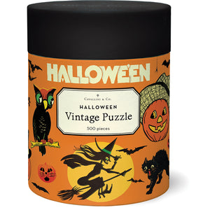 The Halloween Vintage 500 Piece Puzzle by Cavallini Papers and Co features vintage witches, black cats, owls, bats, and jack-o’-lanterns on a festive orange background in a round container.