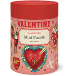 A cylindrical red and pink Cavallini Papers and Co box labeled "Valentine Mini Puzzle, 240 pieces" features vintage Valentine’s Day art and heart motifs.