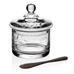 The Jasmine Covered Honey Jar with Spoon by William Yeoward Crystal features a clear glass jar with an engraved lid and comes with a small palm wood spoon, all displayed against a white background.