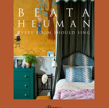 The cover of the book “Beata Heuman, Every Room Should Sing” by Rizzoli showcases a vibrant bedroom designed by acclaimed interior designer Beata Heuman, highlighting a blue dresser, patterned bed, custom furnishings, and a whimsical wall mural that reflects her playful Scandinavian style.
