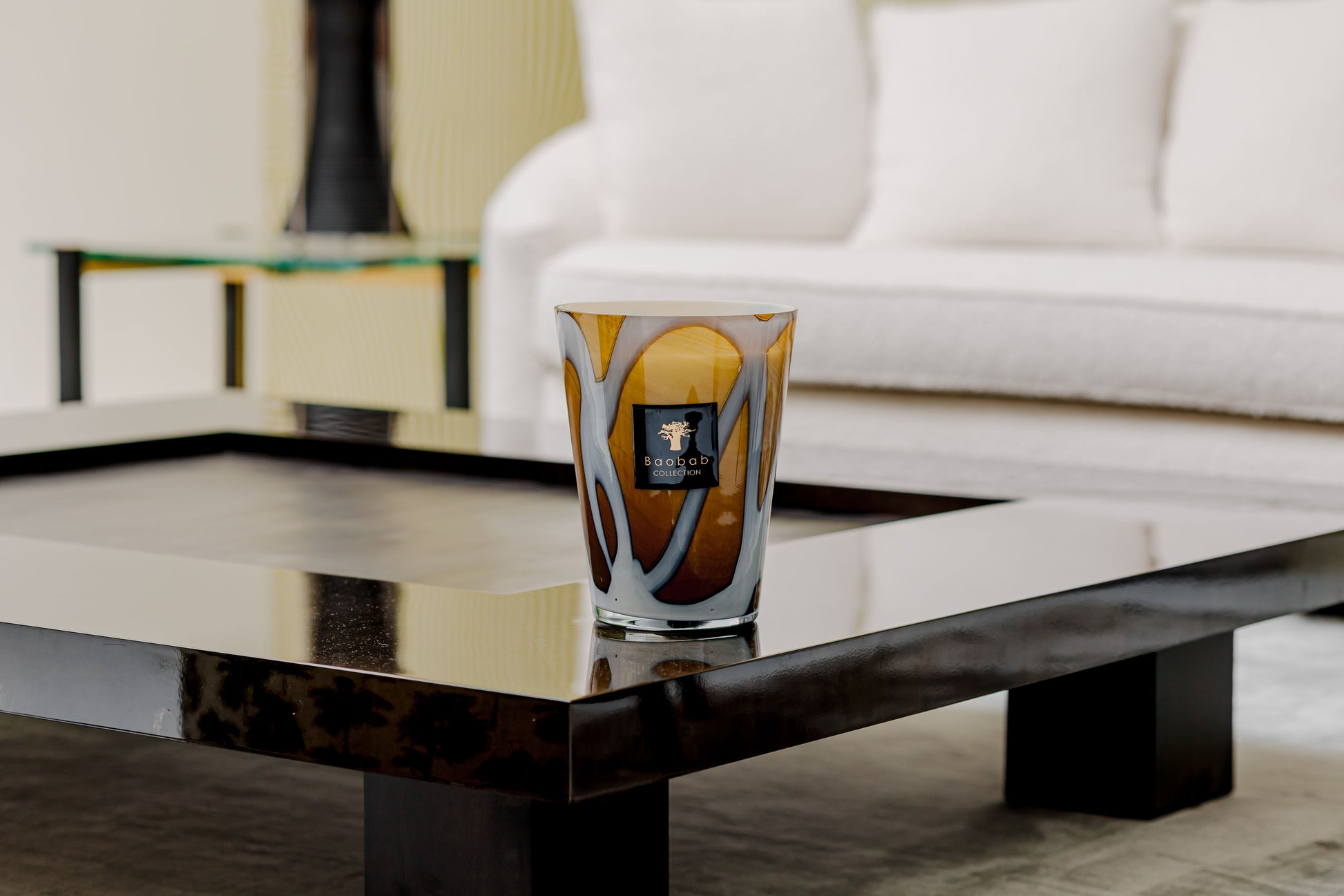 Artistic glass tumbler on a sleek black coffee table accompanied by a Baobab Collection Stones Agate Candle in a modern living room setting.