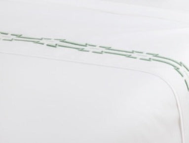 A close-up of Yves Delorme’s Couture Tuileries Bedding Collection shows luxe white PIMA cotton percale with a decorative green stitched border in a curved, repeating pattern near the edge.