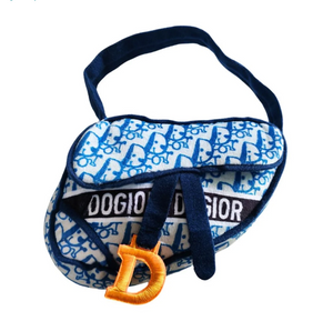 The Haute Diggity Dog Dogior Navy Saddle Bag Dog Toy features a blue and white pattern, navy strap, black "DOGIOR DOGIOR" label, and yellow "D" charm—perfect for carrying your pup’s favorite plush squeaker toy on the go.
