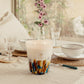 A large Baobab Rainforest Mayumbe scented candle on a table set with dishes and glasses, near a floral arrangement, in a warm, well-lit room.