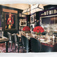 An open spread from Ralph Lauren A Way of Living by Rizzoli features a sophisticated dining room with a polished table, black chairs, vibrant red floral centerpieces, bookshelves, and framed artwork against dark walls—an elegant showcase of Ralph Lauren’s home interior style.