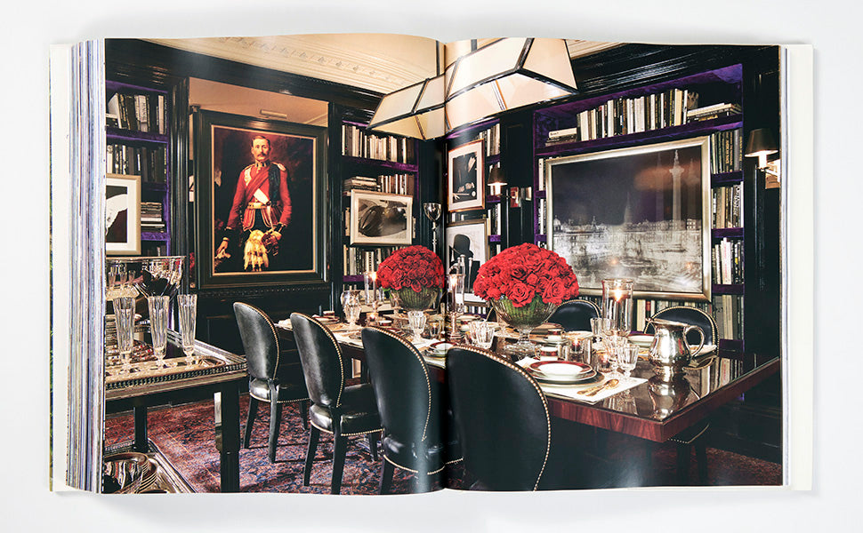 An open spread from Ralph Lauren A Way of Living by Rizzoli features a sophisticated dining room with a polished table, black chairs, vibrant red floral centerpieces, bookshelves, and framed artwork against dark walls—an elegant showcase of Ralph Lauren’s home interior style.