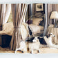 Two long-haired dogs lie on the floor beside a canopied bed in a lavishly decorated bedroom with neutral tones and elegant furnishings, capturing the refined aesthetic showcased in *Ralph Lauren: A Way of Living* by Rizzoli.